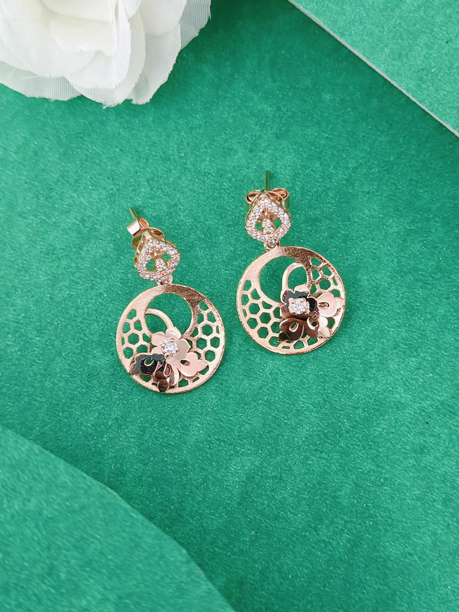 Rose gold earrings with floral designs on a green background